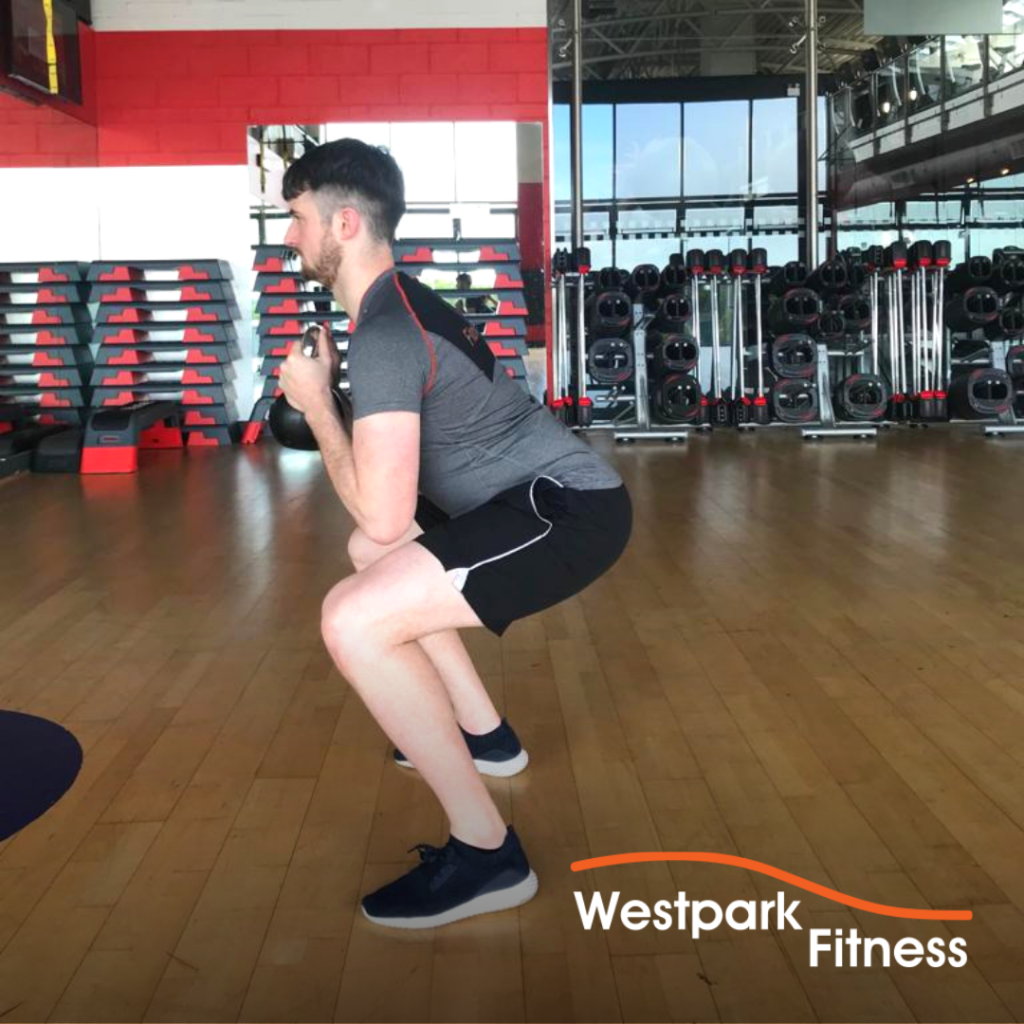male gym goer in a squat position holding a kettlebell to complete the goblet squat exercise at westpark fitness