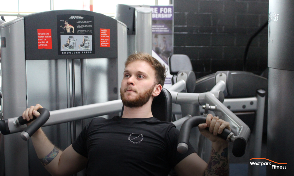 shoulder press machine exercise at westpark fitness male gym goer sitting on machine with handles down at his shoulders