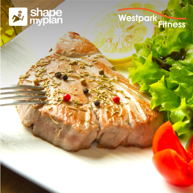grilled tuna steak on a white plate beside a lemon and tomato and lettuce leaves